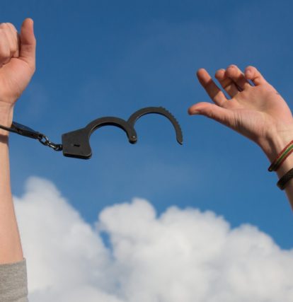 handcuffs breaking off two hands reaching up towards the sky